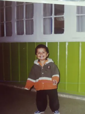 Issa as a kid, grinning in front of a green wall